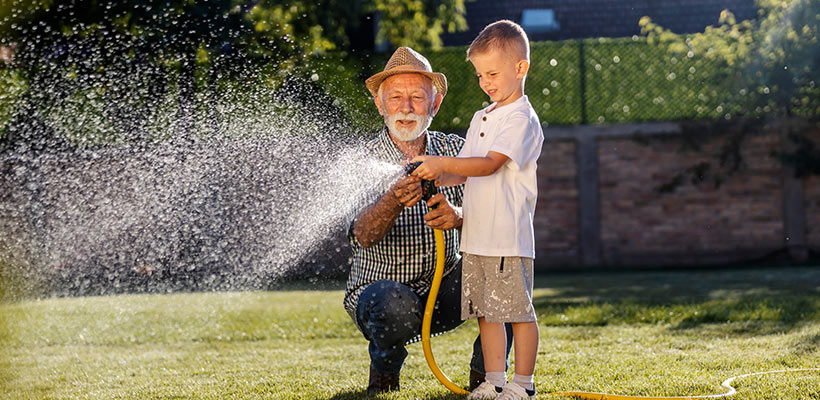 Man watering the lawn with his grandson.