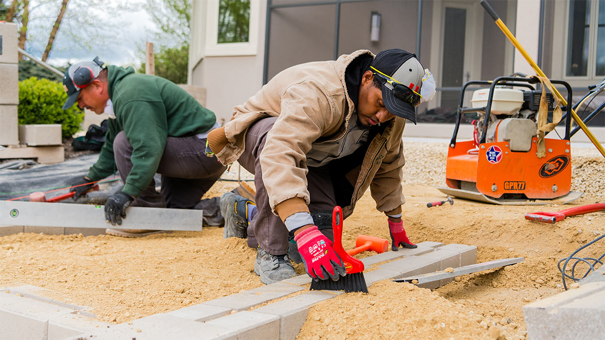 LawnCare by Walter hardscaping crew carefully laying retaining wall blocks and leveling paver stones.